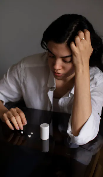 Woman sitting with medication pills and showing signs of emotional distress